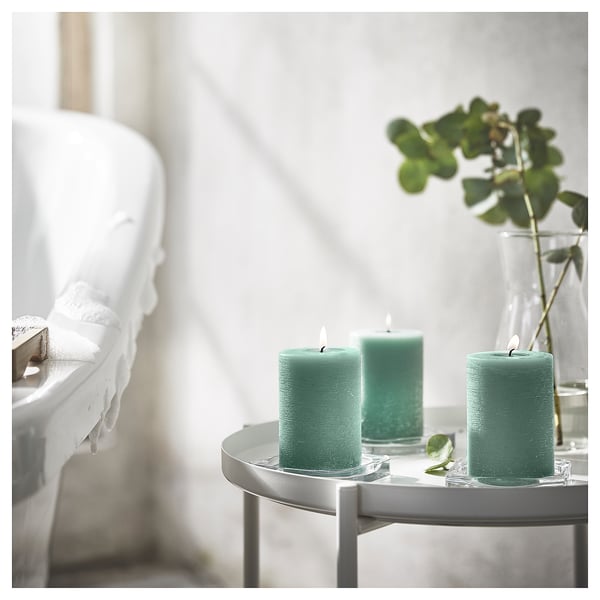 Green candles on white table, beside white bathtub with towels.