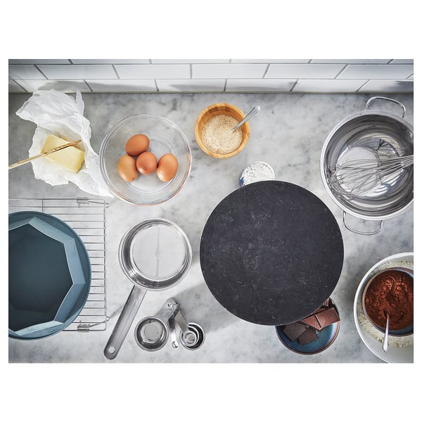 A blue baking bowl, kitchen tools, and a rotating black cake stand on a marble countertop.
