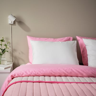 Minimalist bed with BÄRGLIM white pillow, pink comforter, white nightstand, and vase.