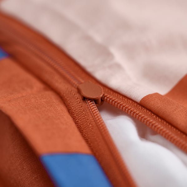Close-up of an orange zip on a kids jacket, showing a pull tab and part of the fabric.