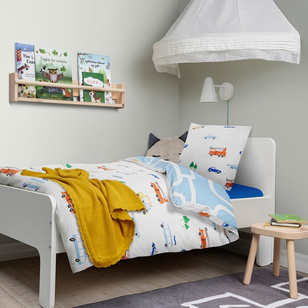 Bedroom with BERGFINK blue/white vehicle duvet, yellow blanket, bookshelf, stool, and white canopy.