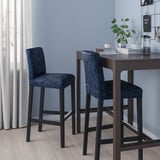 Blue bar stools under dark counter with plant, cups, & books.