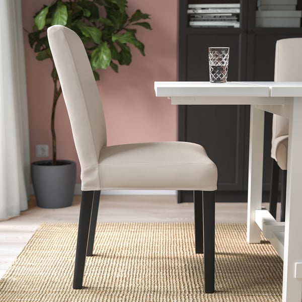 A dining area with a beige upholstered chair and a glass on a white table.