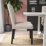 A dining area with a beige upholstered chair and a glass on a white table.