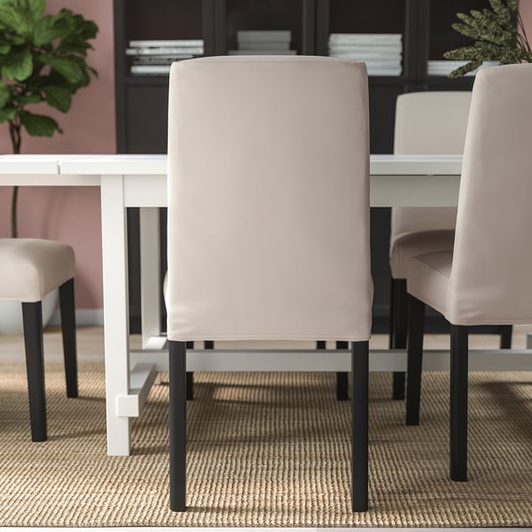 Modern dining setup with upholstered chairs around a white table. Chairs have beige covers and black legs, offering comfort and style.