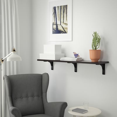 Explore a BERGSHULT wall shelf, black, with one bevelled & one smooth edge, displaying books & a plant next to a grey chair & small table.