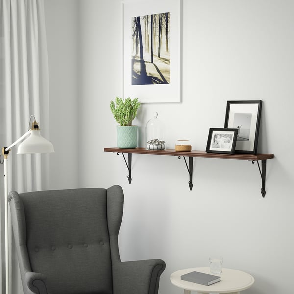 Cozy corner: grey chair, white side table, berry shelf with plant, photos, & decor. Shelf mounted on white wall, framed forest art above.