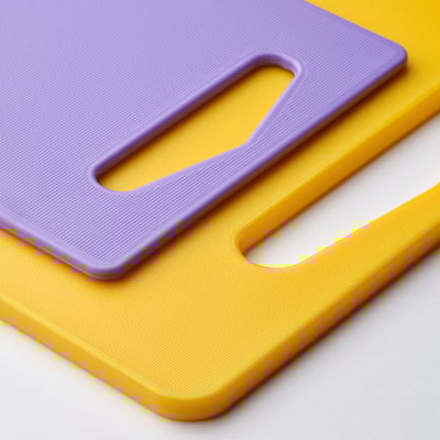 Yellow & purple cutting boards with handles on a flat surface.