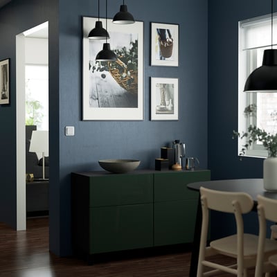 Modern dining area with dark blue walls, green BESTÅ sideboard, hanging lights, framed photos, white chairs, and a wooden floor.