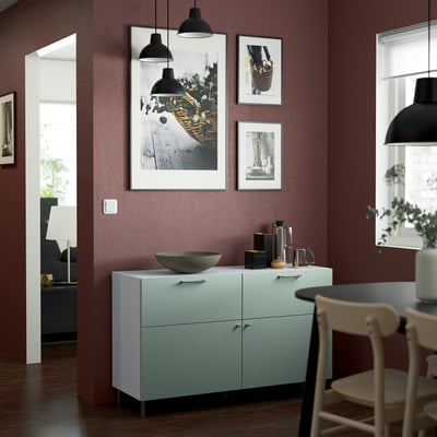 Modern living room with maroon walls, largeBESTÅ sideboard in white, wooden bowl, decorations. Hanging paintings, black pendants, plant.
