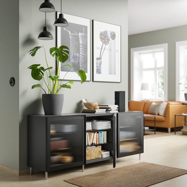Modern living room with black BESTÅ unit, books, plant, decor, and orange seating.