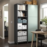 Modern home office with BESTÅ storage, dark shelves, wooden desk, black chair, green cabinet.