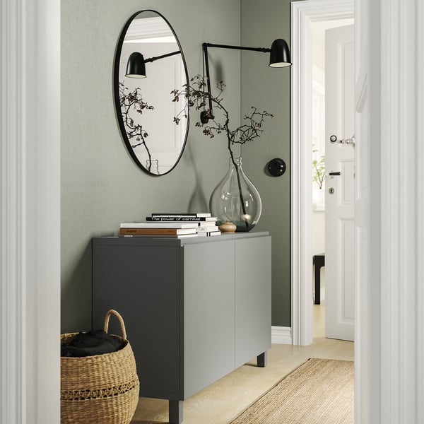 Hallway with green walls, BESTÅ unit, mirror, vase, basket, wall lights, white door.
