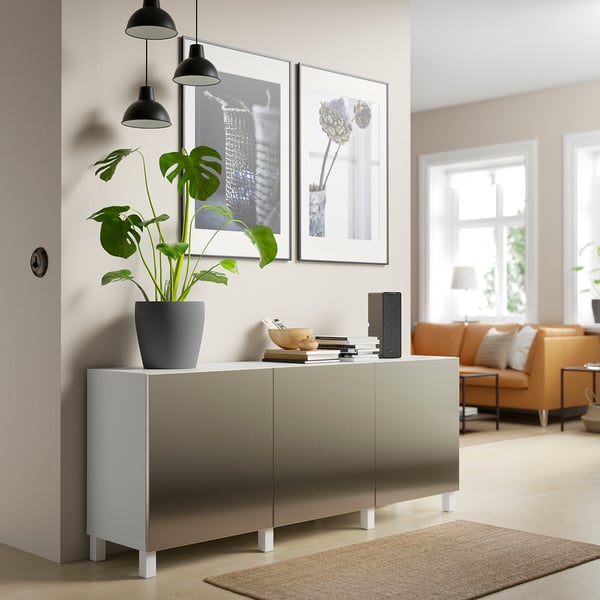Modern living room with BESTÅ silver sideboard, plant, decor, black lamps, art, and orange sofa.