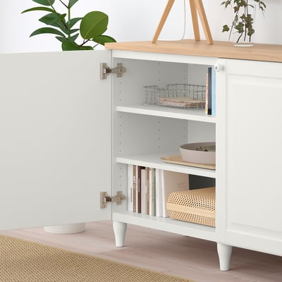 A white BESTÅ sideboard with open doors revealing shelves holding baskets and books, showcasing its storage and organizational.