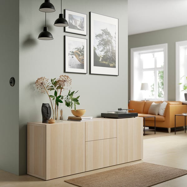 Light wooden BESTÅ sideboard, sleek & minimalist, fits under hanging pictures, with decorative vases, near orange sofa.