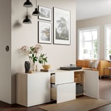 Modern storage unit with open drawers and shelves, holding decorative vase, bowl, books, and records. Hanging art and floor lamp above.