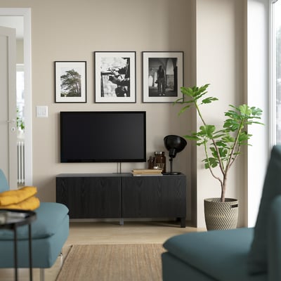 Modern living room with BESTÅ tv stand, flat screen, teal chairs, black lamp, yellow throw, plant, and black & white frames.