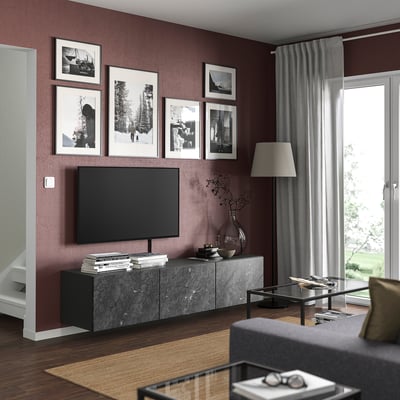 Modern living room with dark red walls, grey furniture, black tv, framed photos, grey curtains, wooden floor, and glass coffee table.