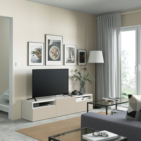 Modern living room with BESTÅ white tv bench, flat screen, decorative frames, grey curtains, and glass coffee table.