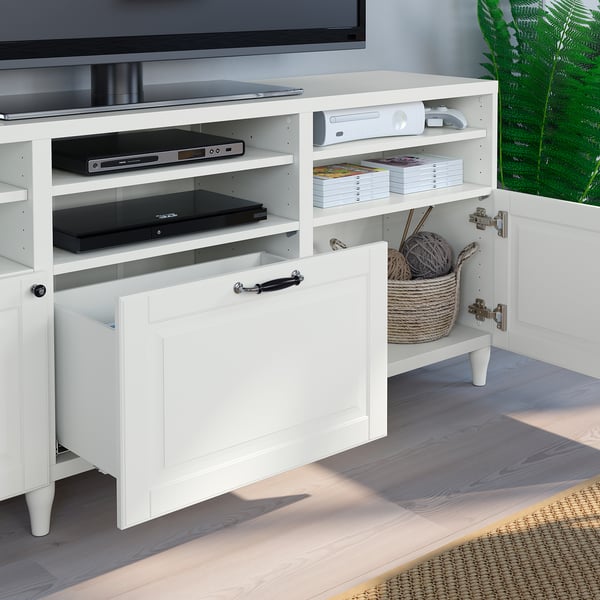 White BESTÅ tv stand with open drawer, visible cables, and adjustable shelves storing electronics and books.