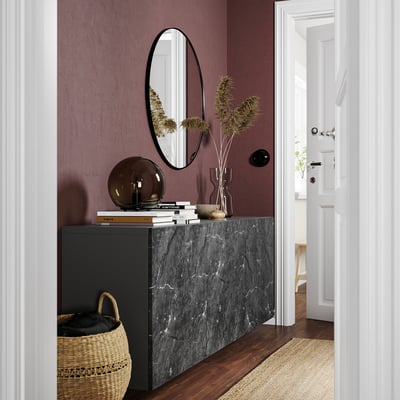 Modern entryway with dark purple wall, black marble console, round mirror, dried flowers, woven basket, and white door.