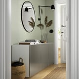Gray BESTÅ cabinet with mirror and dried flowers in hallway.