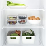 Well-organized fridge with stacked glass food containers, storing fruits and leftovers. Transparent design for easy identification and space-saving.