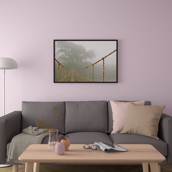 A cozy living room with a gray sofa, a wooden coffee table, and a framed poster of a wooden suspension bridge in foggy forest.