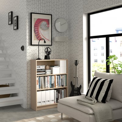 Modern living room with BILLY bookcase, comfy couch & guitar. Wall clock & framed art. Large window.