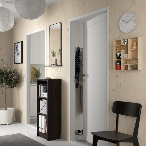 A modern hallway with a black BILLY bookcase and minimalist decor, including a wall clock and wooden shelves.