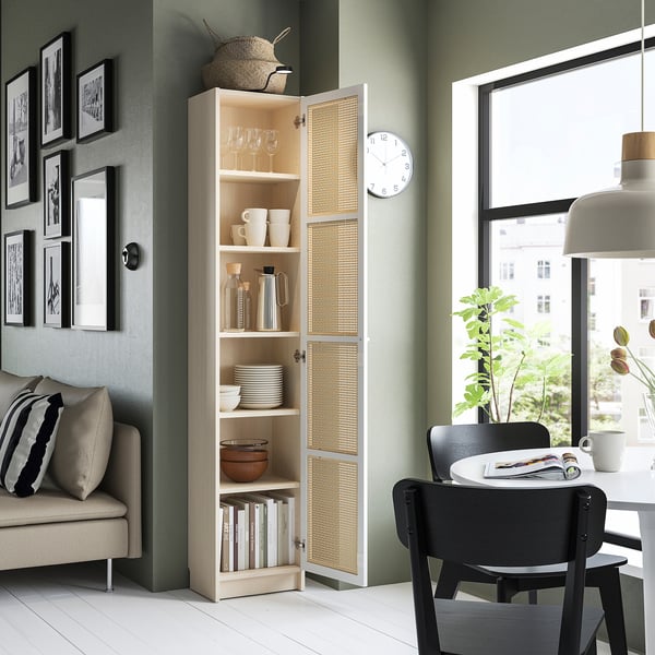 Modern living room with tall beige BILLY bookcase, black dining chairs, white table, green wall, and window.