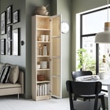 Modern living room with tall beige BILLY bookcase, black dining chairs, white table, green wall, and window.