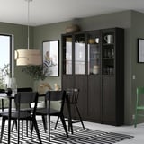 Modern dining room with a tall black BILLY bookcase filled with glassware. It stands next to a black table and chairs with a large window nearby.