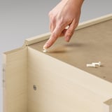 Persons hand adjusting white hinge on light-colored BILLY bookcase.