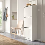 Modern hallway with white BISSA shoe cabinet, light pink chair, hanging jacket, and shelf with bottle.