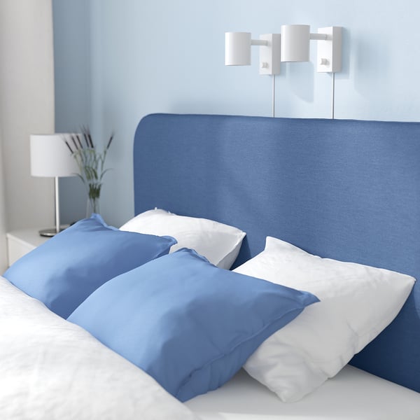 Blue bed with white sheets, two wall lamps, and a bedside table with a bouquet.