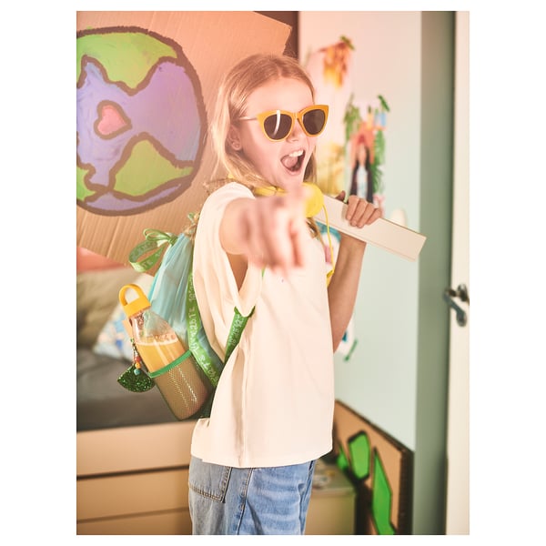 Girl with yellow BLÅVINGAD backpack in colorful room.