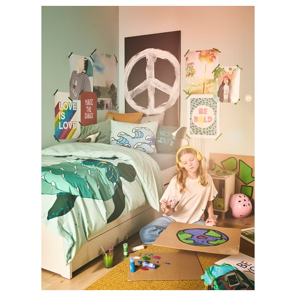 Child draws on bed with ocean-themed decor and colorful supplies.