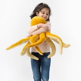 In a child hugs a large yellow plush octopus toy. The toy has soft, long tentacles and is part of the BLÅVINGAD collection.