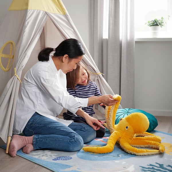 Woman and child play indoors with a soft toy octopus. They are inside a tent, enjoying the pretend adventure.