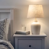 Bedside lamp with ceramic base, brass, & beige shade.