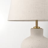 Modern table lamp with a textured cream base, brass accents, and a white fabric shade, exuding a warm, inviting glow.