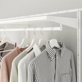 Closet with clothes hangers, striped shirt, beige sweaters, white hangers, white shelves, and hanging rod.