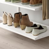 White wall-mounted shelves storing various footwear. Brown zipper boots, beige block heels, and light green slip-ons are neatly organized.