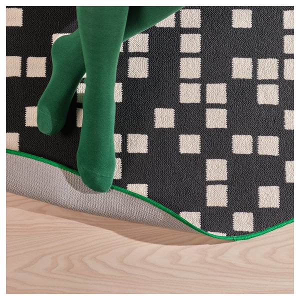 A persons feet wearing green socks on a gaming rug with a black and white pixel pattern, emphasizing the rugs quality and design.