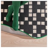 A persons feet wearing green socks on a gaming rug with a black and white pixel pattern, emphasizing the rugs quality and design.