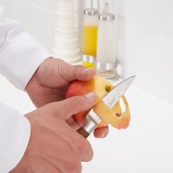 Person peeling apple with metallic knife, revealing its sharp edge and durable blade.