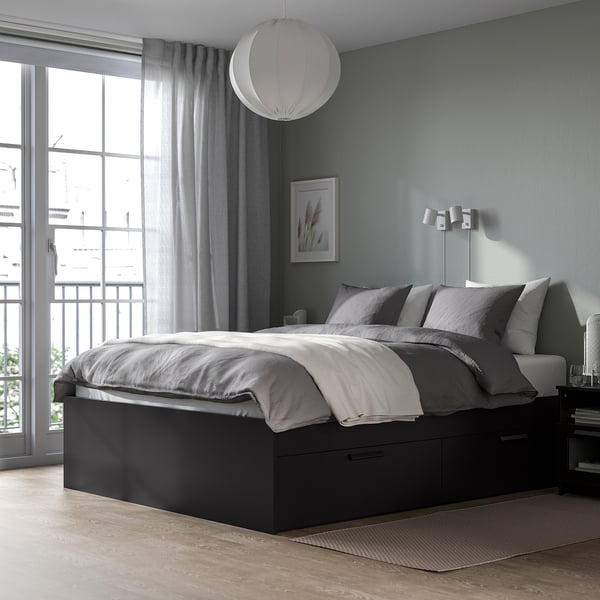 Modern bedroom with black BRIMNES bed, grey linens, large window, light grey curtains, round pendant lamp, and wall-mounted reading lights.