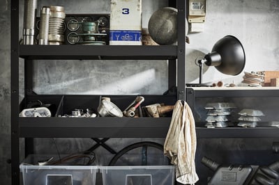 Black metal storage unit with various tools and containers on shelves. Includes a wall-mounted black lamp.
